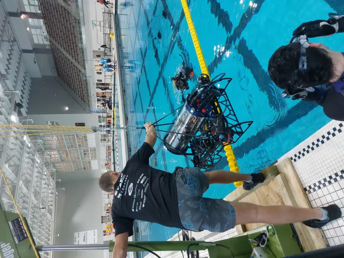 An Autonomous Underwater Vehicle (AUV) is lowered into a swimming pool July 31, 2022, for the 2022 RoboSub competition in College Park, Maryland. RoboSub is an international robotics competition, where student teams design, build, test and operate their own robotic submarines—AUVs—in challenging underwater environments. (Courtesy Photo)