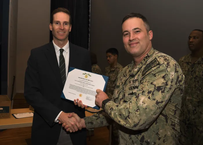 ason Payne (left), director, ONR Global TechSolutions, presents Lt. Cmdr. Sam Hughes (right), with the Gold Star, awarded by the Secretary of the Navy, while ONR Global Executive Officer Capt. Eric Hutter (not pictured), recites the commendation to the audience inside the base theater at Naval Air Station Patuxent River on Oct. 26, 2023. (Photo by Chief Petty Officer Patrick Gordon)
