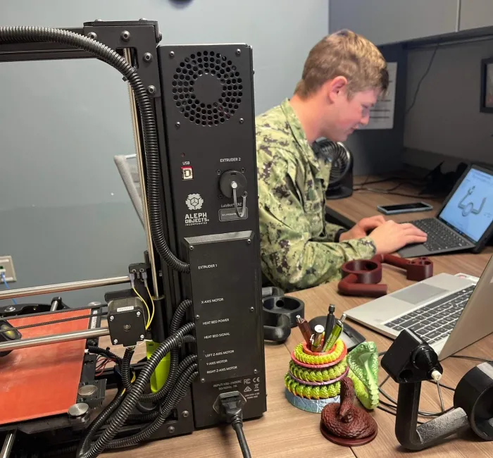 AZ2(AW) Jonathan Ziminski works with 3D printer creating a replica of an E-2D yoke.