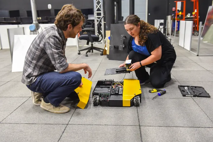 Jordan Doles (right), a Naval Research Enterprise Internship Program (NREIP) intern, and Kyle Hart, Autonomy/AI team lead at the Naval Air Warfare Center Aircraft Division, work on an advanced robot in the Robotics and Intelligent Systems Engineering Lab.